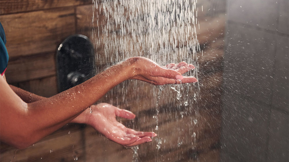 Mulher com a mão embaixo da água do chuveiro