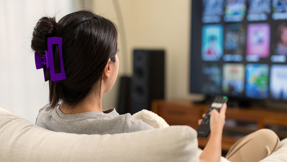 Mulher sentada no sofá com o controle remoto na mão assistindo TV