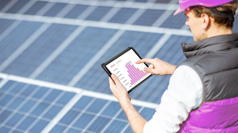 Profissional analisa dados de desempenho solar em tablet sobre painéis fotovoltaicos, representando práticas de gestão energética.