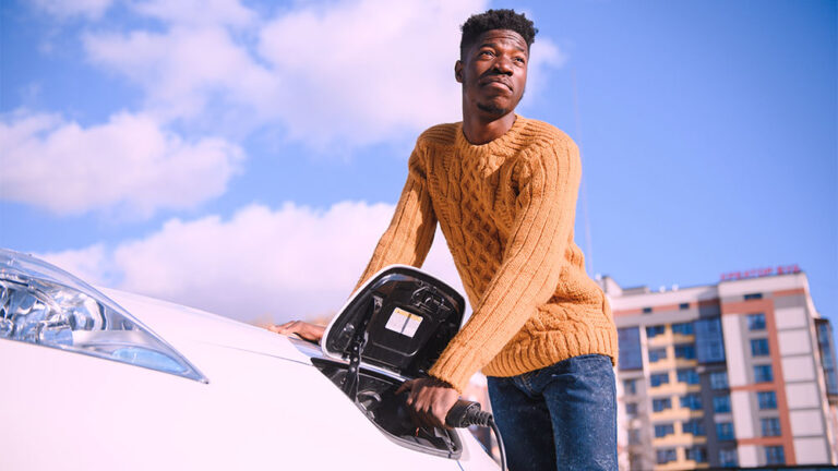 Pessoa conectando cabo de carregamento em automóvel branco, simbolizando o uso de veículos elétricos e a mobilidade sustentável.